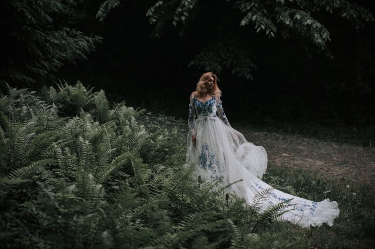 Alternative wedding dress with blue floral embroidery and long sleeves photographed in a romantic forest setting.