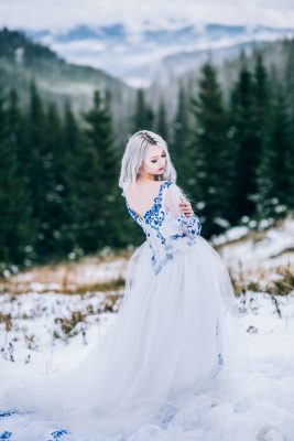 groom in a blue suit and bride in white, embroidered with blue pattern, dress on a background of green pine forests in the mountains of the Carpathians
